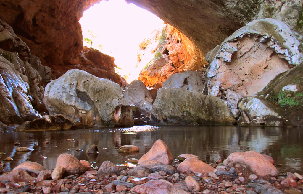 View from inside Tonto Natural Bridge cave showing large rocks and a reflective pool of water.